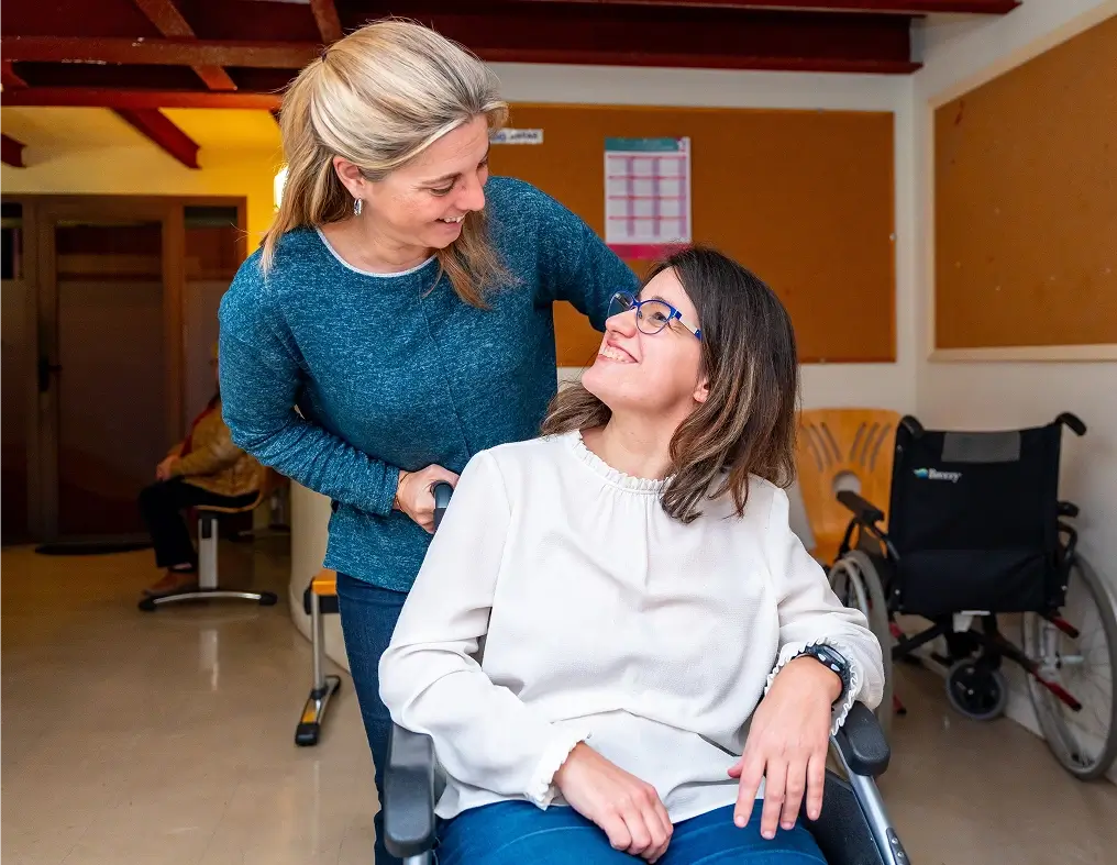 Caregiver pushing the wheelchair of a disabled woman in a day center for people with special needs
