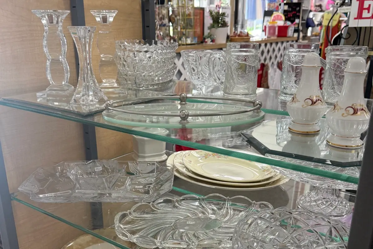 Glassware, serving trays, and decorative tableware displayed on thrift store shelves