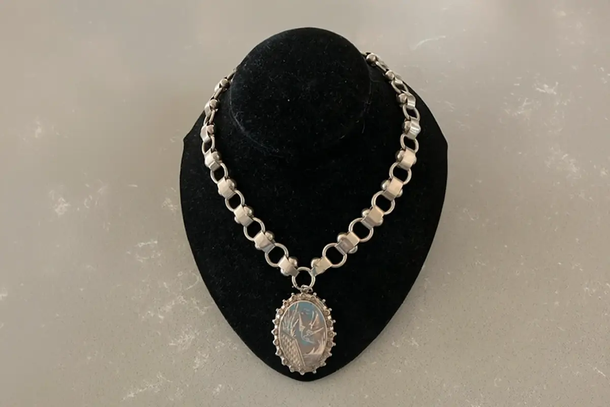 Silver necklace with a blue pendant displayed on a black jewellery stand