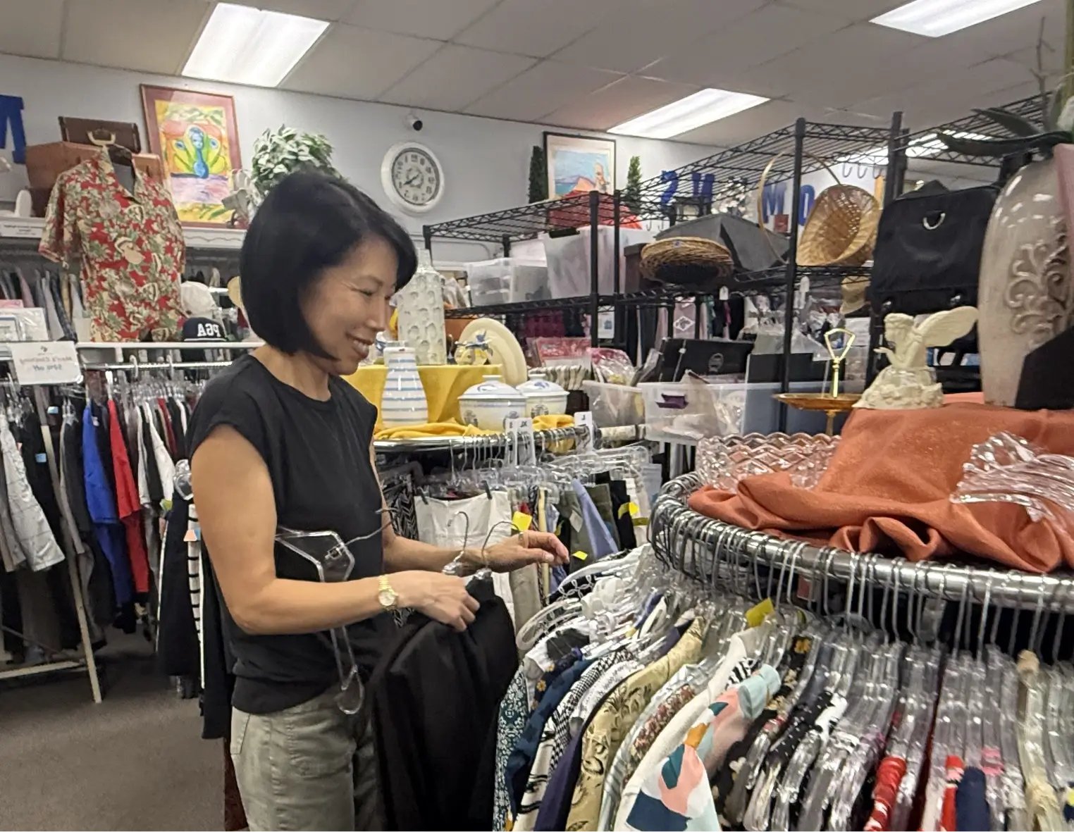 Happy female small business owner in denim apron checking clothing rack in fashion boutique