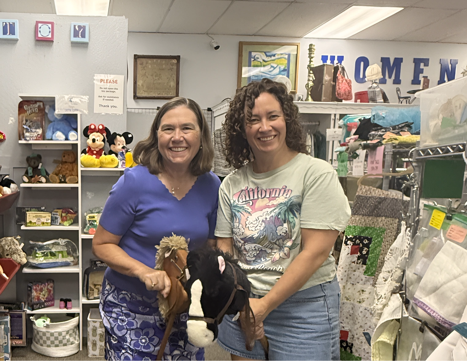 Two women posing with stuffed horses in a shop